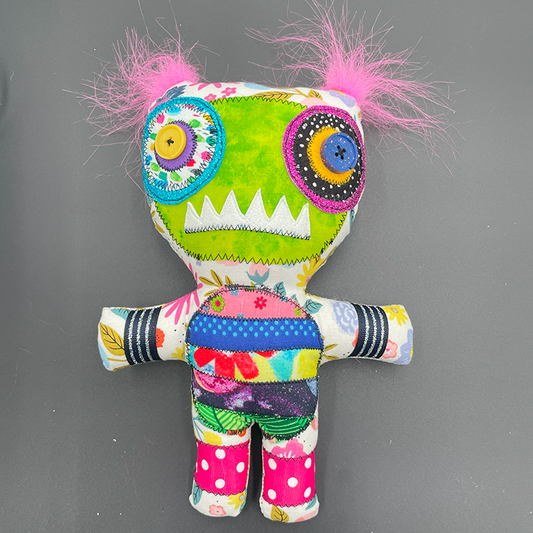 A decorative monster doll with a floral and polka-dot patterned shirt, green body, and pink hair.
