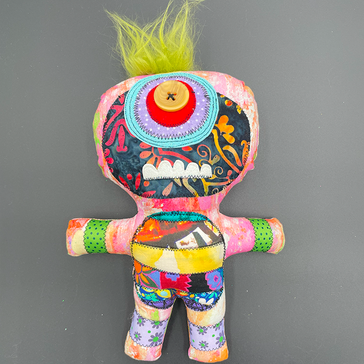 A colorful art doll with a monster character design, featuring a variety of fabrics and buttons, with a green hair-like top and a button for an eye.