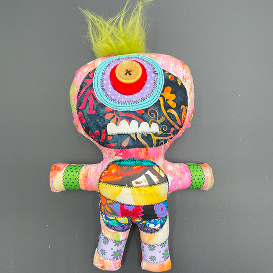 A colorful art doll with a monster character design, featuring a variety of fabrics and buttons, with a green hair-like top and a button for an eye.